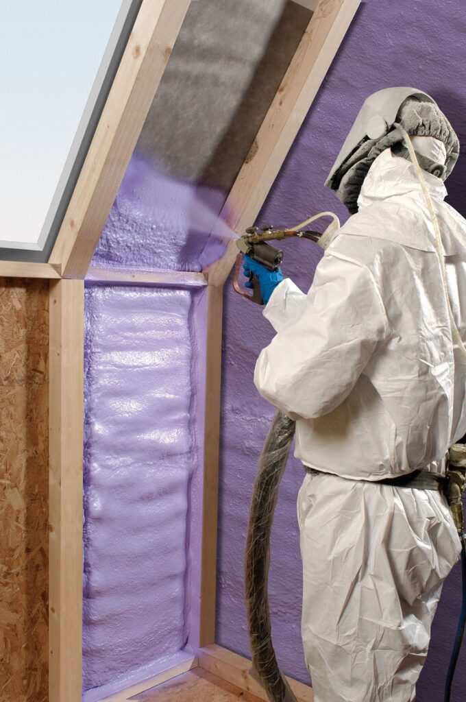 Worker in protective gear applying spray foam insulation to the attic walls of a house, ensuring energy efficiency and thermal control.